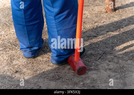 Close-up of construction worker's blue workwear pants leg and red sledgehammer Stock Photo
