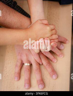 Close up top view of family holding hands stacked together on wooden table. Concept of unity, support, protection, family values, love, and bonding of Stock Photo