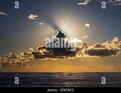 Brilliant sunset over the open sea with sunbeams breaking from behind a dark triangular cloud. Stock Photo