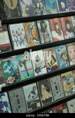 Rows of dusty vintage Thai pop cassette tapes with colorful album covers displayed on a wooden shelf in Chiang Mai, Thailand Stock Photo