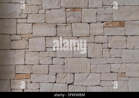 Natural limestone wall constructed from irregular rectangular stone blocks, showing rough surfaces, subtle beige tones and traditional masonry texture Stock Photo