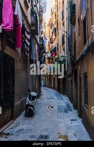 Barcelona, Spain - 01 December 2025: View of a narrow, stone-paved street with tall residential buildings, laundry hanging from balconies, and a parke Stock Photo