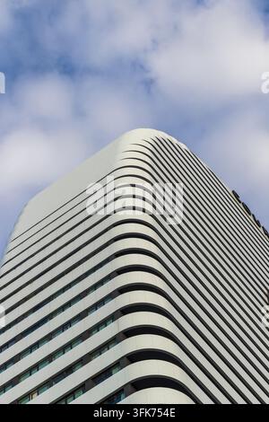 Low angle vertical view of a modern skyscraper facade featuring a geometric pattern of curved white balconies. Stock Photo