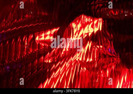 Abstract background of crumpled shiny metallic foil with warm red and orange light reflections, modern futuristic design, textured surface Stock Photo