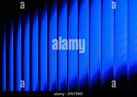Abstract photo of vibrant blue neon light shining through vertical corrugated panel texture or window blinds. Concept of cyber security, modern archit Stock Photo