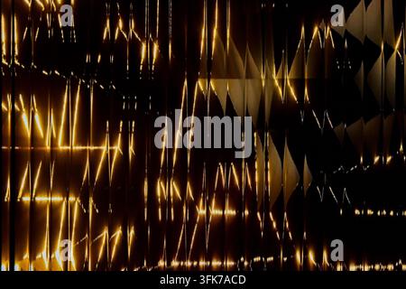 Abstract full frame photo of warm golden amber light and geometric triangle shadows shining through vertical fluted corrugated glass panel. Concept of Stock Photo