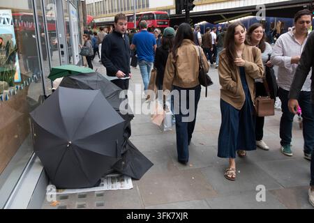 Sleeping rough a person seeks shelter sitting on the ground behind three umbrellas so she / he can not be seen or  identified, crowds of people shopping in the Kings Road, Chelsea walk on past. England 2026 2020s UK HOMER SYKES Stock Photo