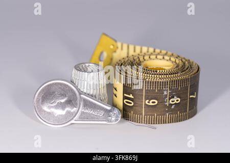 Collection of sewing accessories including tape measure, thimble and needle threader on a neutral background. Stock Photo