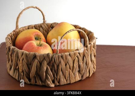 Fresh apples in small woven basket placed on brown texture surface, studio shot Stock Photo
