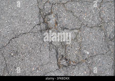 Top view of cracked asphalt pavement with detailed damaged surface and rough gravel texture. Stock Photo
