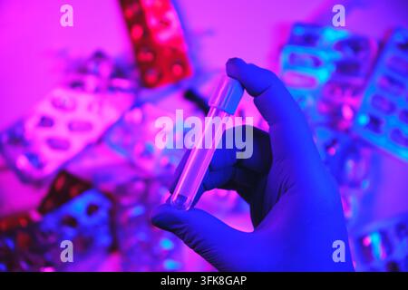 Hand in medical glove holding a clear test tube against a background of drug blister packs Stock Photo