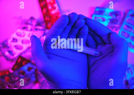 Gloved hands holding a test tube, conducting research in a neon-lit laboratory environment Stock Photo
