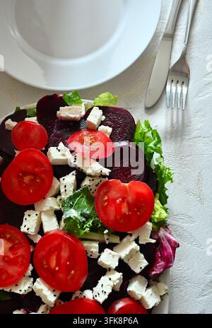 Fresh healthy beetroot salad with feta cheese, tomatoes, and green lettuce served on a white tablecloth, top view flat lay. Stock Photo
