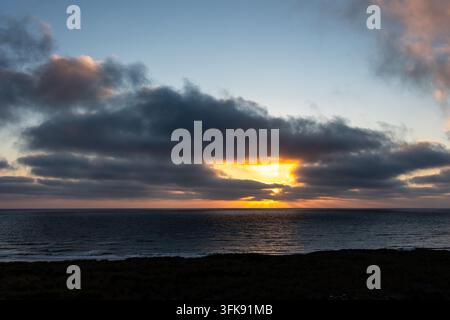 Golden sunbeams bursting through a dark, cloudy sky and reflecting on the calm ocean surface, creating a peaceful and dramatic natural scene during su Stock Photo