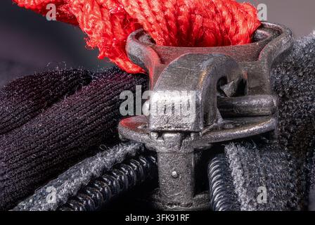 Macro view showing a metal zipper puller with a vibrant red rope attached, closing the textured black fabric, highlighting industrial hardware and det Stock Photo