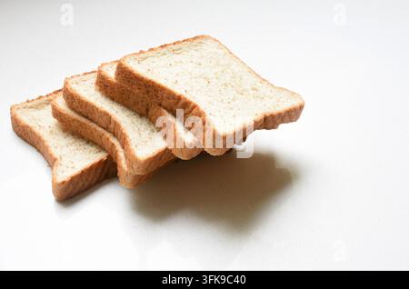 Fresh slices of whole wheat sandwich bread arranged on a clean white table. Simple food composition representing healthy eating, nutrition, breakfasst Stock Photo