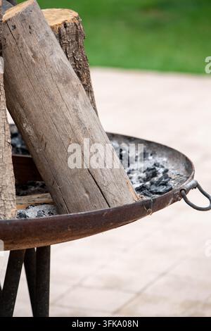 Stone fire pit with stacked firewood in a landscaped garden, outdoor recreation area. Rustic circular stone fire pit filled with stacked firewood Stock Photo