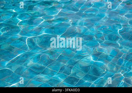 Close-up view of crystal clear swimming pool water with sunlight reflections illuminating the tiled bottom, creating a vibrant turquoise texture. Stock Photo