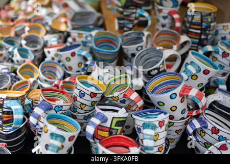 Colorful collection of handmade ceramic mugs with diverse hand-painted patterns, dots, and hearts on display Stock Photo
