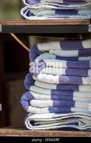 Stack of neatly folded blue and white pool towels on a wooden shelf at a hotel swimming pool. Clean fresh towels prepared for guests at a luxury resor Stock Photo