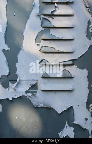 Detailed close-up of peeling white paint on an old weathered metal surface with ventilation louvers Stock Photo