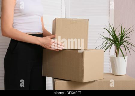 Moving house and relocation logistics, woman holding cardboard boxes for packing and shipping in a new home interior with a houseplant Stock Photo