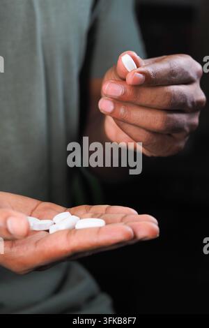 Man holds small white tablets in one hand while using the other hand to pick up one Stock Photo