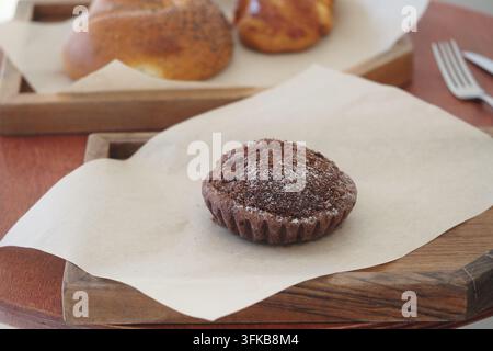 Chocolate muffin on a wooden tray with pastry rolls in background Stock Photo