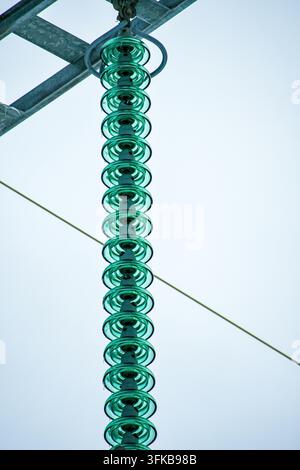 Close-up of a long string of green glass insulators on high-voltage electrical transmission infrastructure. Stock Photo