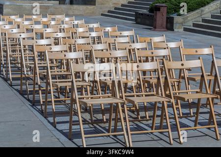 Rows of wooden folding chairs arranged outdoors on a paved area beside a set of steps. Stock Photo