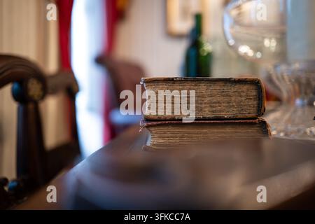 Close up view of two old antique books stacked on wooden table with aged paper edges, wooden chair, and soft indoor room lighting in shallow depth of Stock Photo