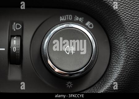 Macro photograph of a vehicle dashboard control panel featuring a rotary headlight switch knob with chrome trim, fog light button, and headlight level Stock Photo