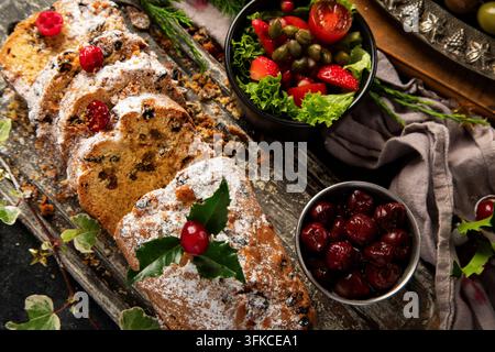 Christmas holiday table setting featuring roasted chicken, salad, assorted snacks, olives and pine branches on a dark background. Top view. Stock Photo