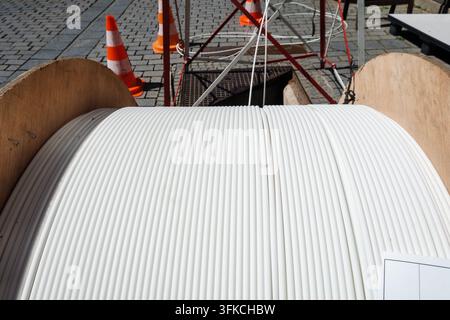 A large reel of white fiber optic cable is positioned on a city street. Construction cones and equipment are visible nearby. Stock Photo