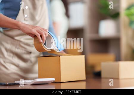 Person sealing cardboard box with tape for small business ecommerce fulfillment Stock Photo