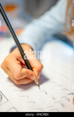 First grade student practices writing letters with pencil in workbook. Early literacy and handwriting skills develop with selective focus and shallow Stock Photo