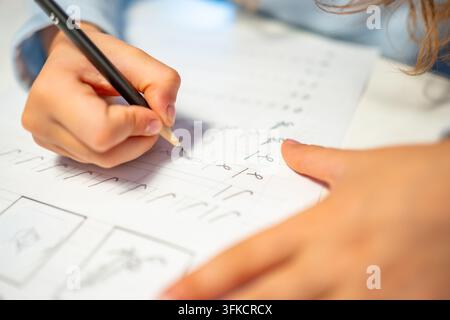 First grade student practices writing letters with pencil in workbook. Early literacy and handwriting skills develop with selective focus and shallow Stock Photo