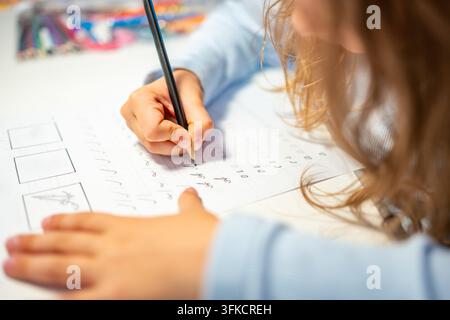 First grade girl practices handwriting with pencil in school workbook. Child learns to write letters during early education with selective focus and Stock Photo