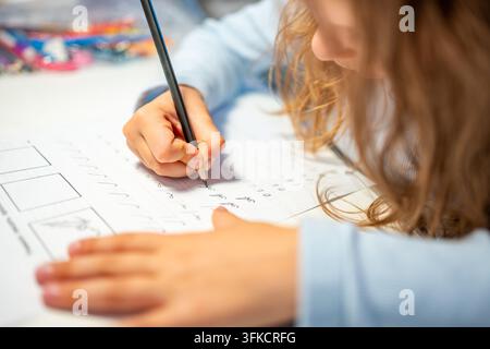 First grade girl practices handwriting with pencil in school workbook. Child learns to write letters during early education with selective focus and Stock Photo