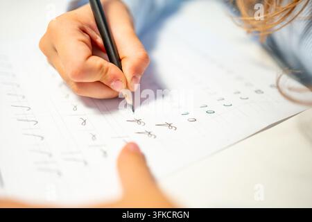 First grade student practices writing letters with pencil in workbook. Early literacy and handwriting skills develop with selective focus and shallow Stock Photo
