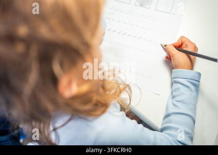 First grade girl practices handwriting with pencil in school workbook. Child learns to write letters during early education with selective focus and Stock Photo