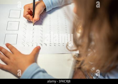First grade girl practices handwriting with pencil in school workbook. Child learns to write letters during early education with selective focus and Stock Photo