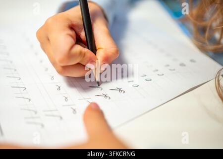 First grade student practices writing letters with pencil in workbook. Early literacy and handwriting skills develop with selective focus and shallow Stock Photo