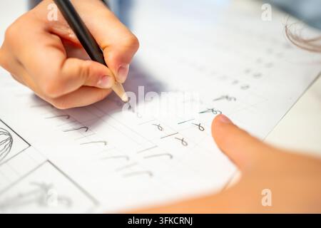 First grade student practices writing letters with pencil in workbook. Early literacy and handwriting skills develop with selective focus and shallow Stock Photo