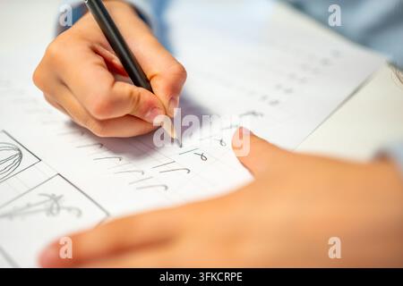First grade student practices writing letters with pencil in workbook. Early literacy and handwriting skills develop with selective focus and shallow Stock Photo