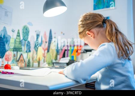 First grade girl practices handwriting at desk in her room. Child studies at home at beginning of school year with selective focus and soft background Stock Photo