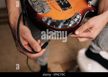 Close-up cropped shot of musician connecting instrument cable to electric bass guitar, plugging in audio jack, preparing for practice, recording Stock Photo