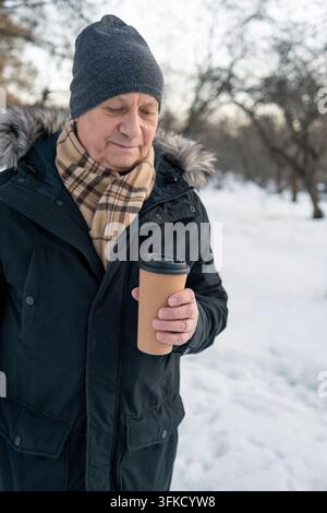Mature man holding takeaway coffee cup in snowy park Stock Photo