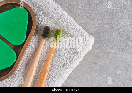 Minimalist flat lay with bamboo toothbrushes, solid shampoo, and white towel on grey surface Stock Photo