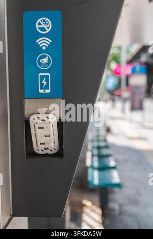 A public charging station displays Wi-Fi, CCTV, no-smoking, and battery symbols beside a softly blurred sidewalk. Stock Photo